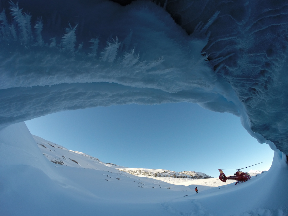 Exit of ice cave looking out towards a red helicopter in the distance.
