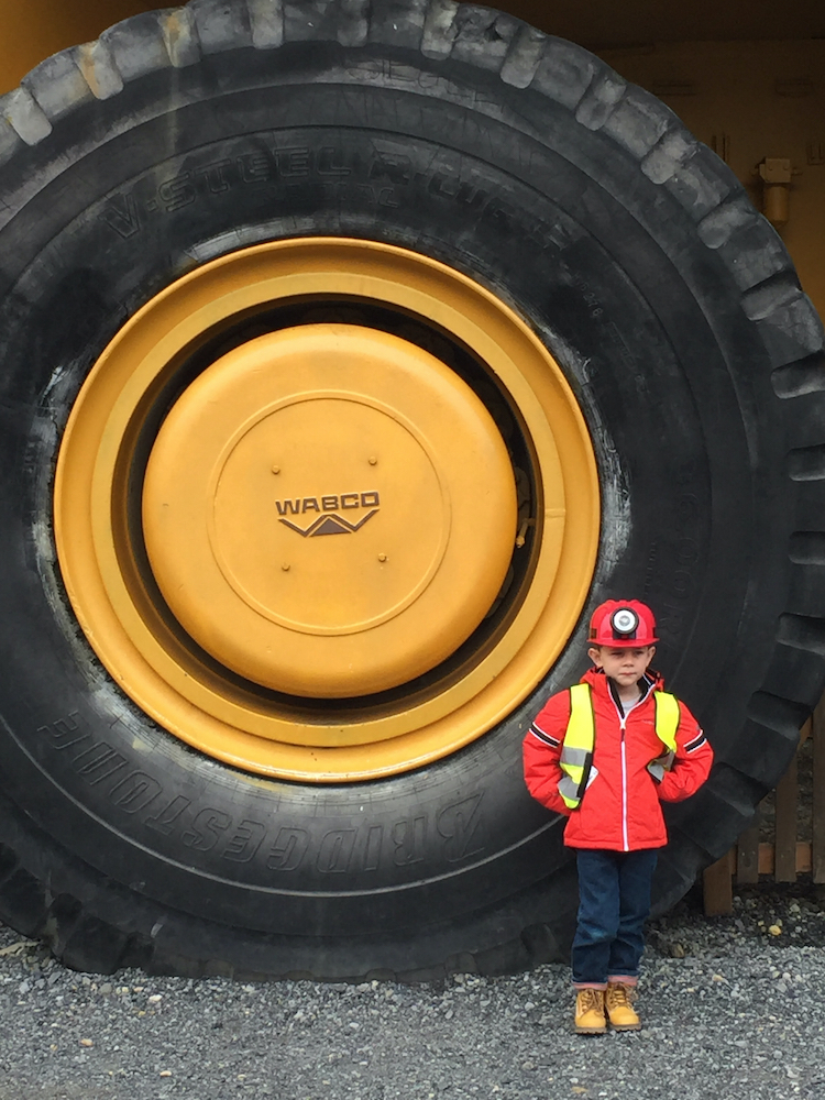 Boy wearing hard hat standing next to wheel of dumper truck at Britannia Mine Museum British Columbia