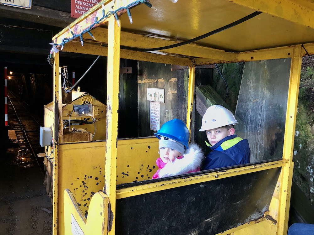 Two children with hard hats sitting inside train at entrance to underground mine at Britannia Mine Museum British Columbia