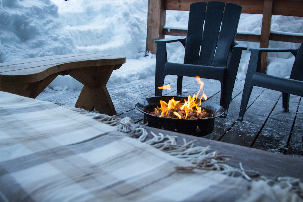 Chairs with blanket next to fire pit surrounded by snow.
